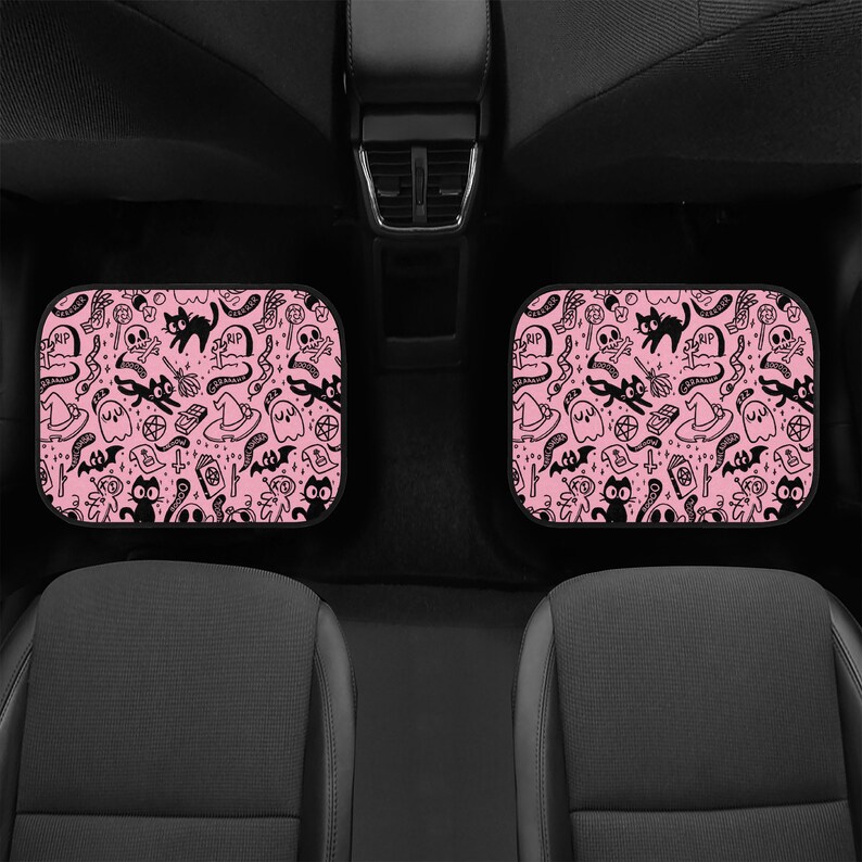May include: Two pink car seat headrests with a black and white Halloween themed pattern. The pattern includes cats, ghosts, bats, skulls, and other spooky symbols.
