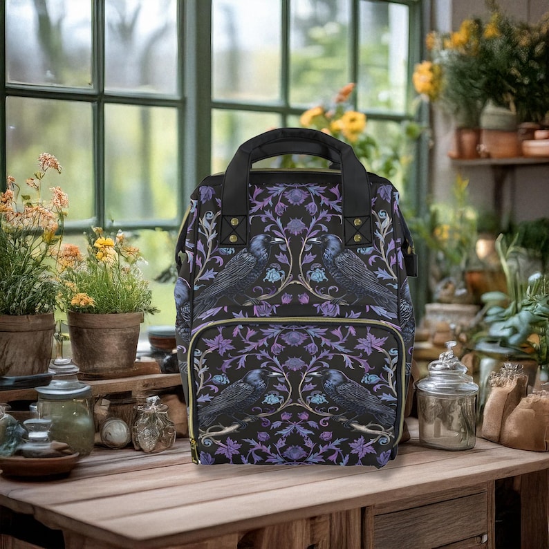 May include: A black backpack with a purple and gold floral pattern featuring birds. The backpack has two adjustable straps and a zipper closure.