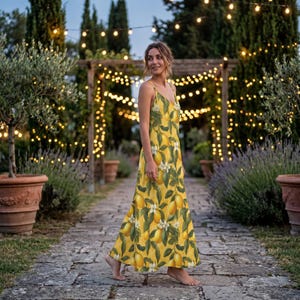 May include: A yellow sundress with a lemon print. The dress has thin straps and a flowing skirt. The background features a stone path, potted plants, and string lights, creating a warm, inviting atmosphere.