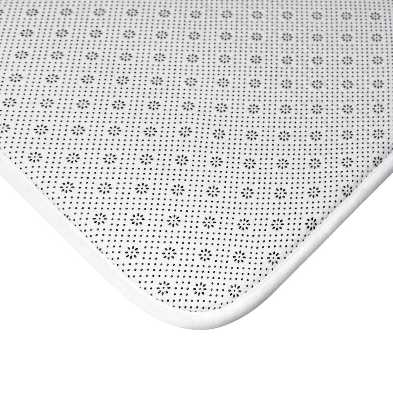 May include: Close-up of the underside of a white bath mat with a black patterned non-slip backing.