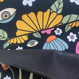 K&ouml;nnte beinhalten: Schwarz-wei&szlig;er Teppich mit einem Retro-Blumenmuster mit gelben, blauen, rosa und wei&szlig;en Blumen. Der Teppich hat auch ein sich wiederholendes Augenmotiv.