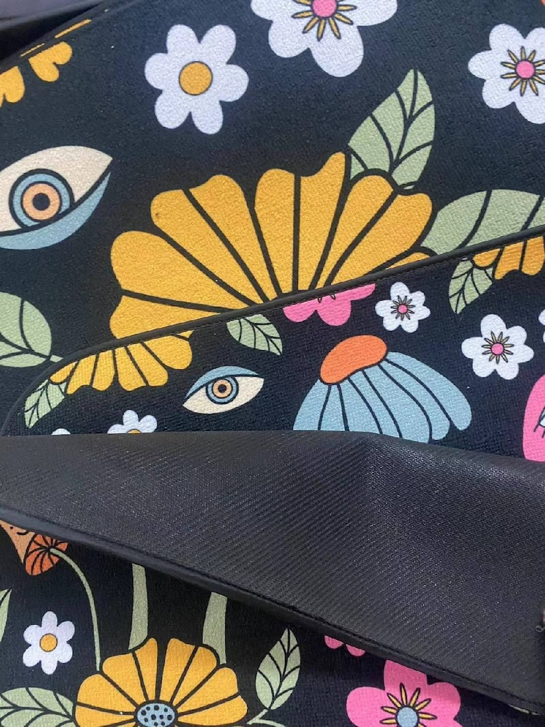 K&ouml;nnte beinhalten: Schwarz-wei&szlig;er Teppich mit einem Retro-Blumenmuster mit gelben, blauen, rosa und wei&szlig;en Blumen. Der Teppich hat auch ein sich wiederholendes Augenmotiv.