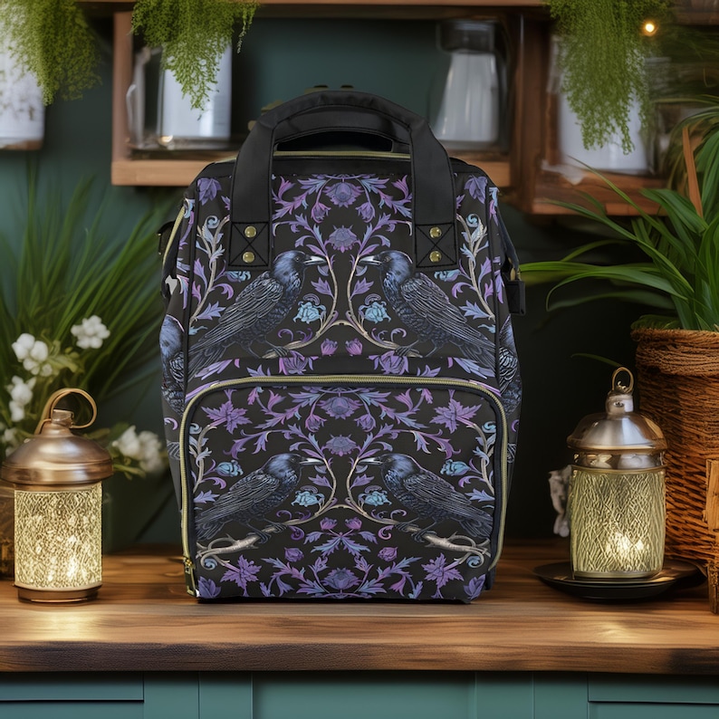 May include: A black backpack with a purple and gold floral pattern featuring black birds. The backpack has a top handle and adjustable straps.