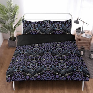 Könnte beinhalten: Ein Bettbezug-Set in Schwarz und Lila mit einem sich wiederholenden Muster aus stilisierten Vögeln und floralen Designs. Das Bettbezug-Set beinhaltet einen Bettbezug und zwei Kissenbezüge.