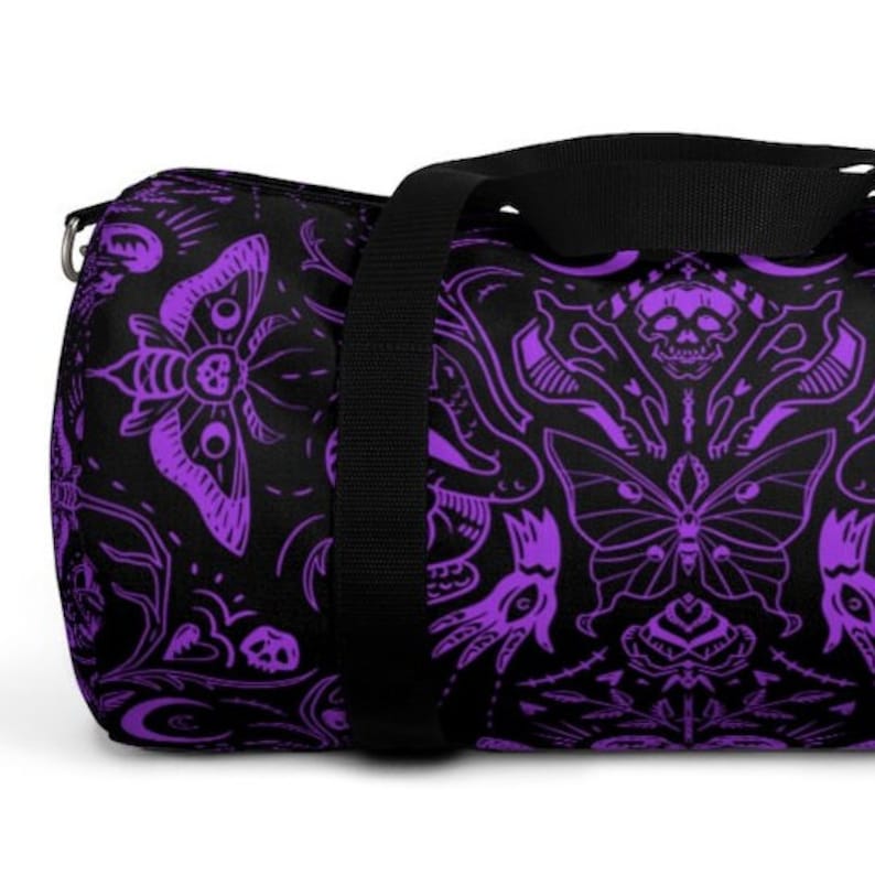 May include: Black duffel bag with a repeating purple pattern of moths, skulls, and floral designs. The bag has a black shoulder strap and a silver-colored metal zipper pull.