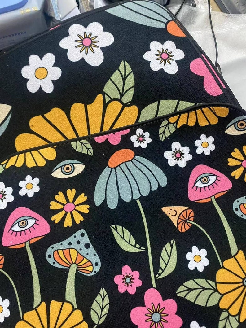 Puede incluir: Alfombra psicod&eacute;lica en blanco y negro con un dise&ntilde;o floral y de hongos. La alfombra presenta flores amarillas, rosas, azules y verdes, as&iacute; como hongos con ojos.