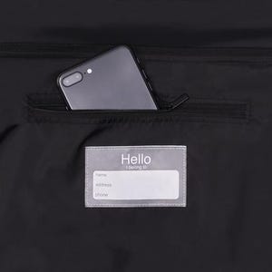 May include: Black bag with a zippered pocket containing a smartphone. A clear label with the word "Hello" and fields for name, address, and phone is visible.