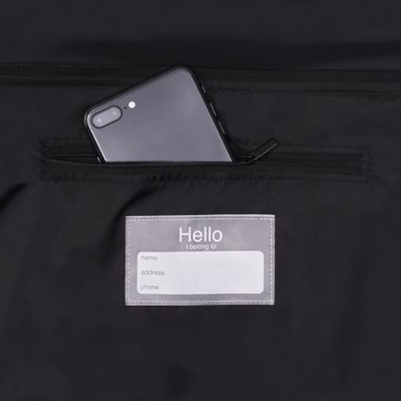 May include: Black bag with a zippered pocket containing a smartphone. A clear label with the word "Hello" and fields for name, address, and phone is visible.