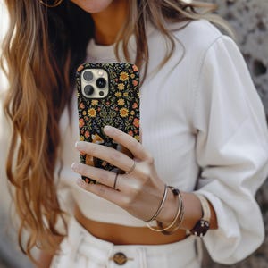 May include: Black phone case with a floral and fox design. The case features a pattern of yellow sunflowers, orange and pink flowers, and green foliage on a black background. The fox is depicted in shades of brown and white.