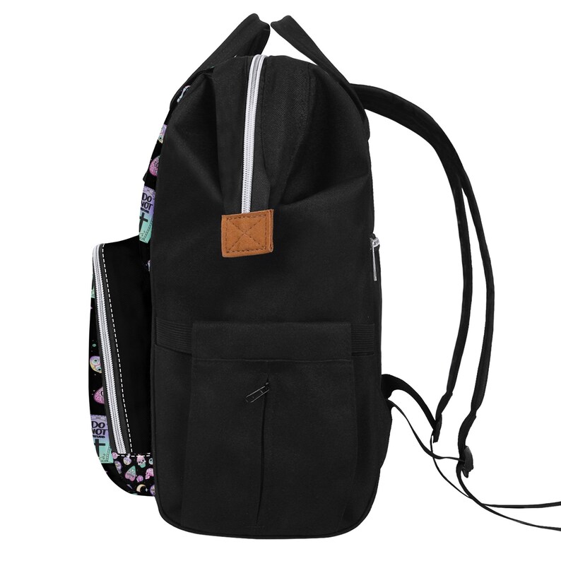 May include: Black canvas backpack with a brown leather patch and a zippered pocket on the front. The backpack has a colorful print on one side featuring various symbols and the text "Do Not Disturb".