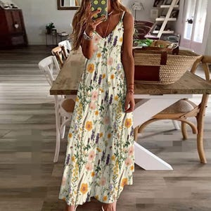 May include: A white maxi dress with a floral print featuring yellow, pink, and purple flowers. The dress has a V-neckline and spaghetti straps.