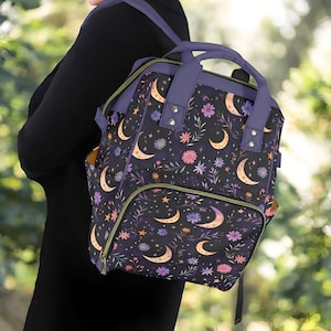 Può includere: Uno zaino viola e nero con un motivo floreale e lune crescenti. Lo zaino ha un grande scomparto principale e una tasca anteriore più piccola.