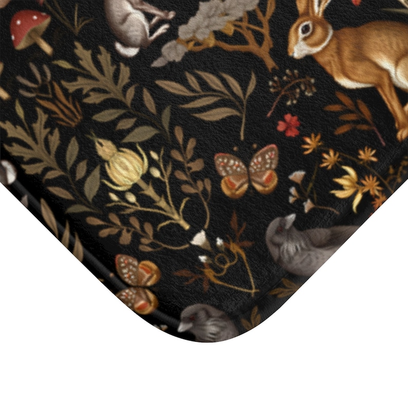 Puede incluir: Una alfombra de ba&ntilde;o negra con un detallado dise&ntilde;o de bosque. El dise&ntilde;o incluye conejos marrones, mariposas, p&aacute;jaros, setas y follaje en tonos marrones, dorados y rojos. La alfombra tiene una superficie texturizada.