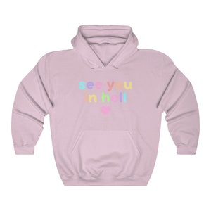 May include: A light pink hoodie with the text "see you in hell" in rainbow colours. A small pink heart is below the text.