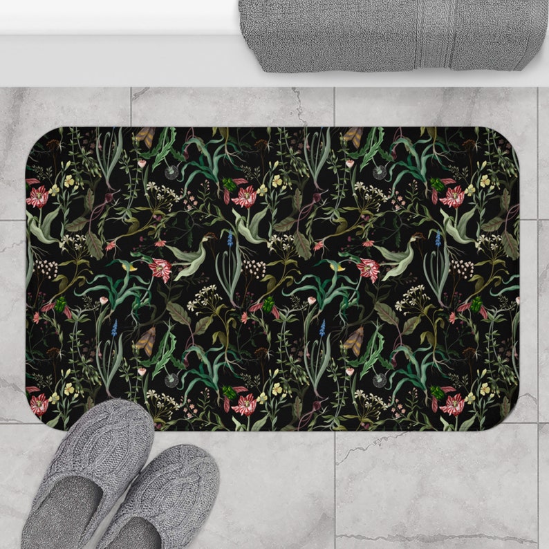 May include: Black bath mat with a floral pattern featuring various flowers and leaves in shades of green, pink, and yellow.