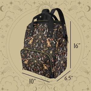 Puede incluir: Una mochila negra con un dise&ntilde;o de estampado de animales del bosque. La mochila tiene una cremallera verde y mide 40,6 cm de alto, 25,4 cm de ancho y 16,5 cm de profundidad.