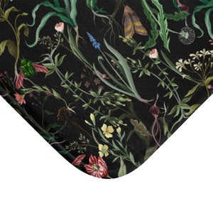 May include: A black bath mat with a floral pattern featuring various flowers, leaves, and insects. The flowers are in shades of pink, red, yellow, and blue. The leaves are green and the insects are black and green.