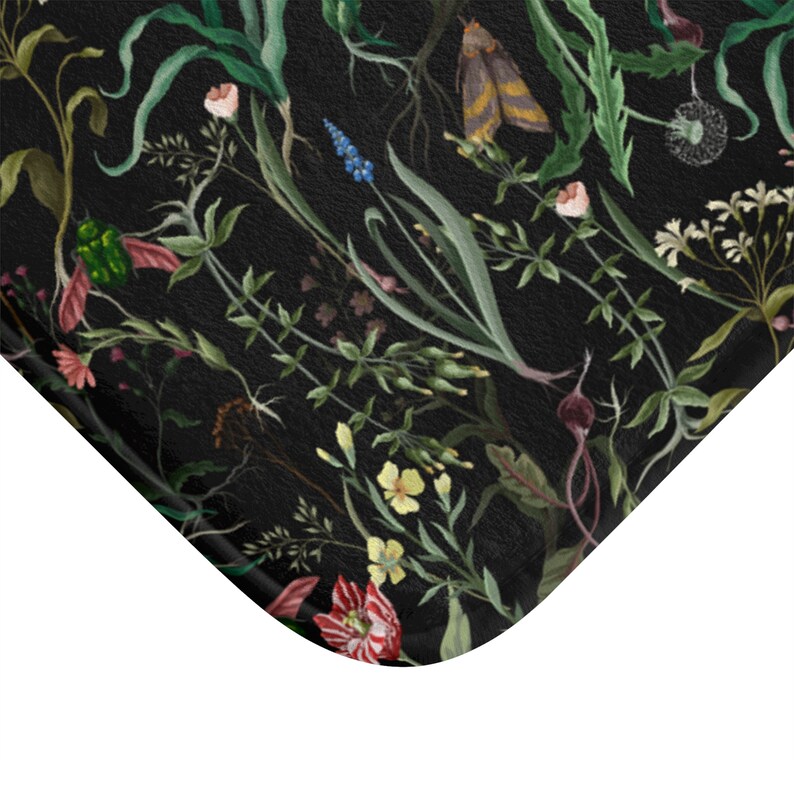 May include: A black bath mat with a floral pattern featuring various flowers, leaves, and insects. The flowers are in shades of pink, red, yellow, and blue. The leaves are green and the insects are black and green.