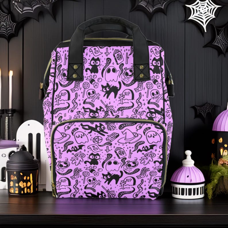 May include: A purple backpack with a black and white Halloween-themed print. The print features cats, ghosts, skulls, bats, and other spooky imagery. The backpack has a black zipper and a black handle.