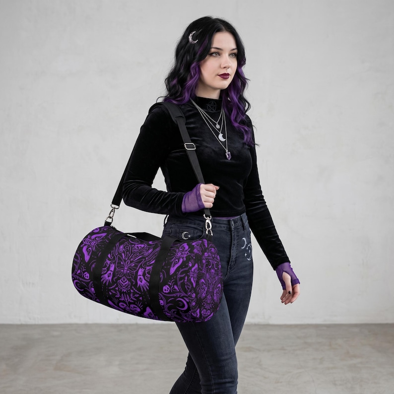 May include: A black and purple duffel bag with a detailed, gothic-inspired pattern. The bag has a cylindrical shape with a black shoulder strap and handles. The design features intricate illustrations in a dark purple hue against a black background, creating a striking contrast.