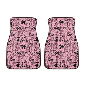 May include: A pair of pink car floor mats with a black and white Halloween themed pattern. The pattern includes ghosts, cats, bats, skulls, and other spooky elements.