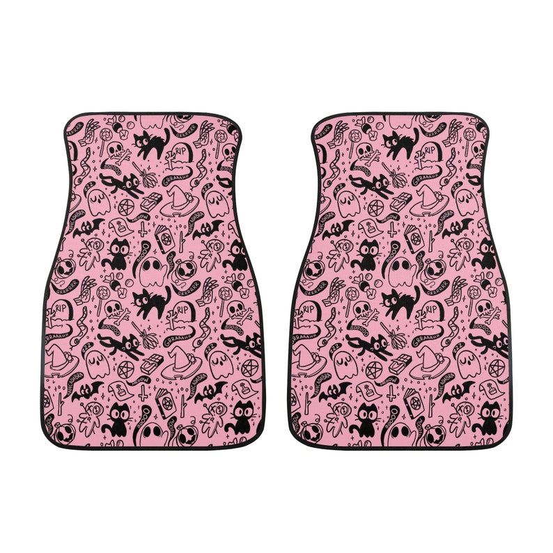 May include: A pair of pink car floor mats with a black and white Halloween themed pattern. The pattern includes ghosts, cats, bats, skulls, and other spooky elements.