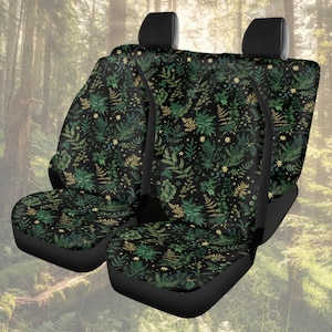 Puede incluir: Dos fundas de asiento de coche negras con un patrón repetido de elementos botánicos verdes y dorados. El diseño incluye helechos, hojas y pequeños acentos en forma de estrella. El fondo es una escena de bosque.