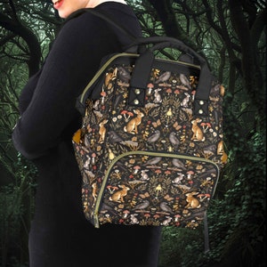 May include: A black backpack with a woodland-themed print featuring rabbits, birds, and mushrooms. The backpack has a large main compartment and a smaller front pocket.