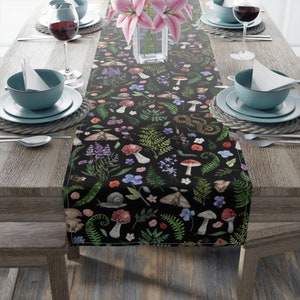 May include: Black table runner with a repeating pattern of mushrooms, ferns, flowers, and insects. The runner is on a wooden table with place settings.