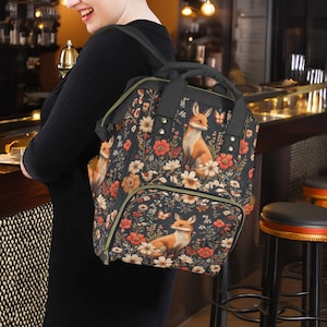 May include: A black backpack with a floral pattern featuring foxes and butterflies. The backpack has a front pocket and adjustable straps.