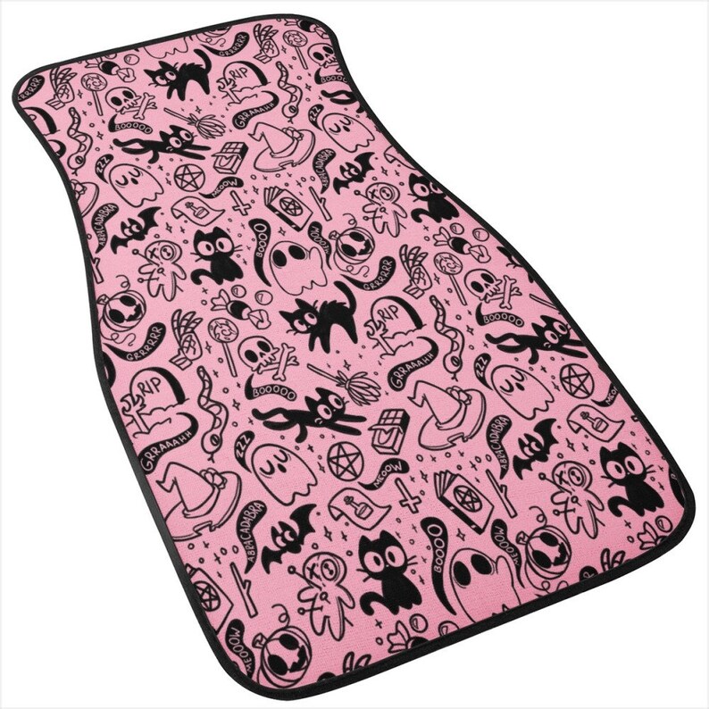 May include: Pink car floor mat with a black and white Halloween themed pattern. The pattern includes ghosts, cats, bats, skulls, and other spooky symbols. The text "GRRAAAHH" and "RIP" are repeated throughout the pattern.
