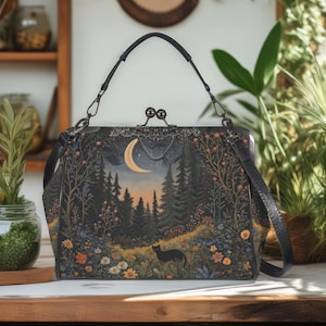 Può includere: Borsa nera con una scena boschiva stravagante con una luna crescente, alberi e un gatto nero. La borsa ha un manico nero e una chiusura decorativa. Il design include fiori e fogliame colorati, creando un'estetica dettagliata e artistica.