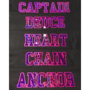 May include: Five iron-on patches with pink and purple glitter lettering. The patches spell out "CAPTAIN", "DEUCE", "HEART", "CHAIN", and "ANCHOR".