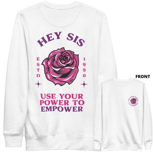 May include: White long-sleeved sweatshirt with a pink rose and the text "Hey Sis Estd 1990 Use Your Power To Empower". The front of the sweatshirt has a small pink rose with the text "Use Your Power To Empower" in a circle.