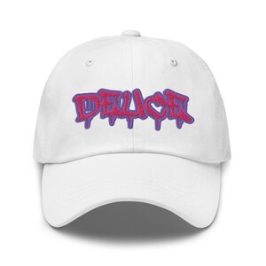 May include: White baseball cap with a pink and purple embroidered "DEUCE" logo in a graffiti style.