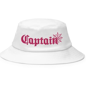 May include: White bucket hat with a pink "Captain" logo and a small pink ship's wheel graphic.