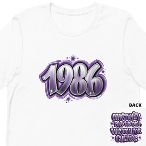 May include: White t-shirt with a purple and silver 1986 graphic on the front. The back of the shirt has the text "Opportunity for Wisdom, Wisdom for Culture" in purple.