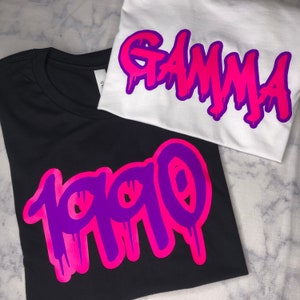 May include: Two t-shirts with a graffiti-style design. One shirt is black with the word "1990" in pink and purple. The other shirt is white with the word "GAMMA" in pink and purple.