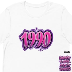 May include: White t-shirt featuring a pink and purple 1990 graphic. The back of the shirt displays the text "Culture is Pride, Pride is Success".