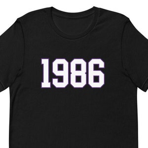 Könnte beinhalten: Schwarzes T-Shirt mit kurzen Ärmeln und weißem Text "1986" in einer fetten, blockartigen Schrift.