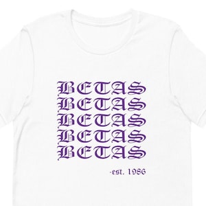 May include: White t-shirt with the text "BETAS" repeated five times in a purple gothic font. The text "est. 1986" is printed below the repeated text.