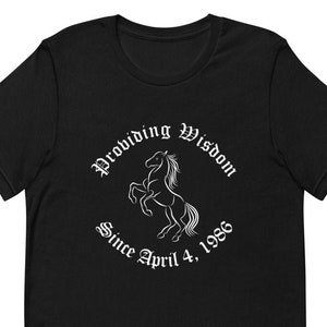 Puede incluir: Camiseta negra con un gráfico blanco de un caballo encabritado con el texto "Providing Wisdom Since April 4, 1986".