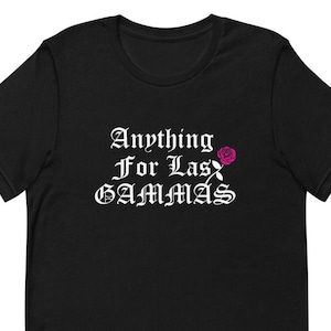 Peut inclure: T-shirt noir avec un texte blanc qui dit "Anything For Las Gammas" avec un graphique de rose rose.