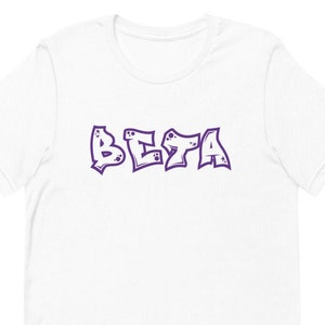 Könnte beinhalten: Weißes T-Shirt mit einem violetten "BETA"-Motiv in einer Graffiti-Schriftart.