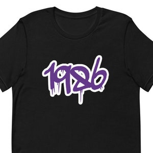 Puede incluir: Camiseta negra de manga corta con un gráfico morado del año 1986 en estilo graffiti.
