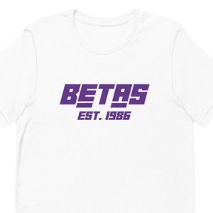 May include: White t-shirt with a purple logo that says "BETAS EST. 1986"