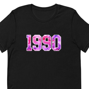 May include: Black short-sleeved t-shirt with a pink and purple watercolor design of the number 1990.