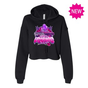 Peut inclure: Sweat-shirt à capuche noir court avec un motif rose et violet d'une voiture et le texte "AMIGAS LAS CAMINAS" avec un design de cristal rose et violet.