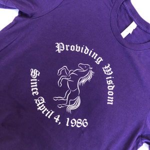 Könnte beinhalten: Lilafarbenes T-Shirt mit einer weißen Grafik eines Pferdes und dem Text "Providing Wisdom Since April 4, 1986".