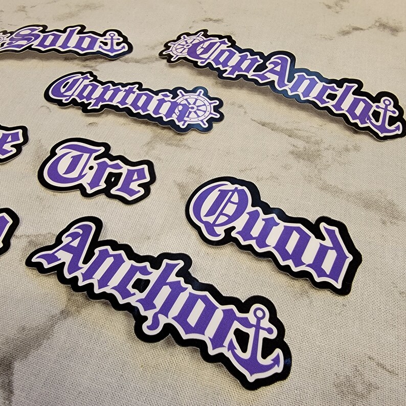 May include: Purple and white vinyl stickers with nautical themes. The stickers feature the words "Solo", "Captain", "Triple", "Quad", and "Anchor" in a gothic font. Some stickers include a ship's wheel or anchor graphic.